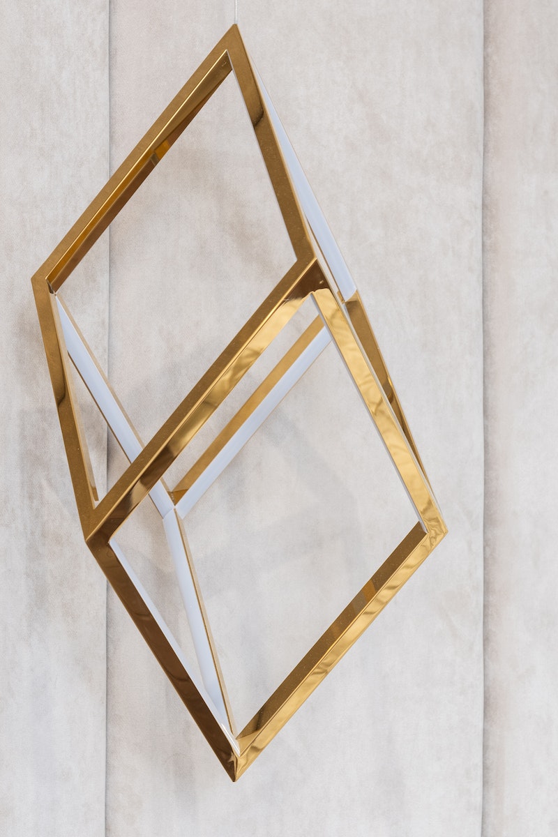 Golden metal geometric cube shaped decor hanging on gray wall in modern apartment